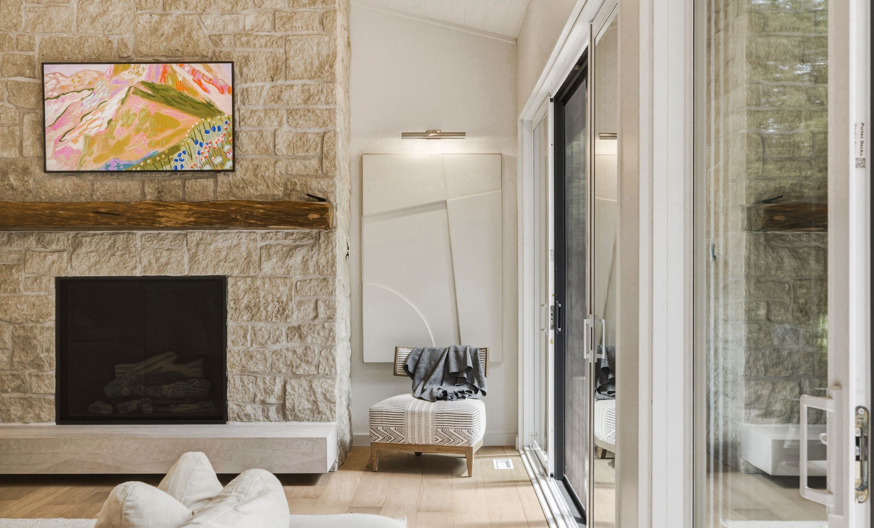 A bright living room with a stone fireplace, timber mantel, and walkout to the deck.