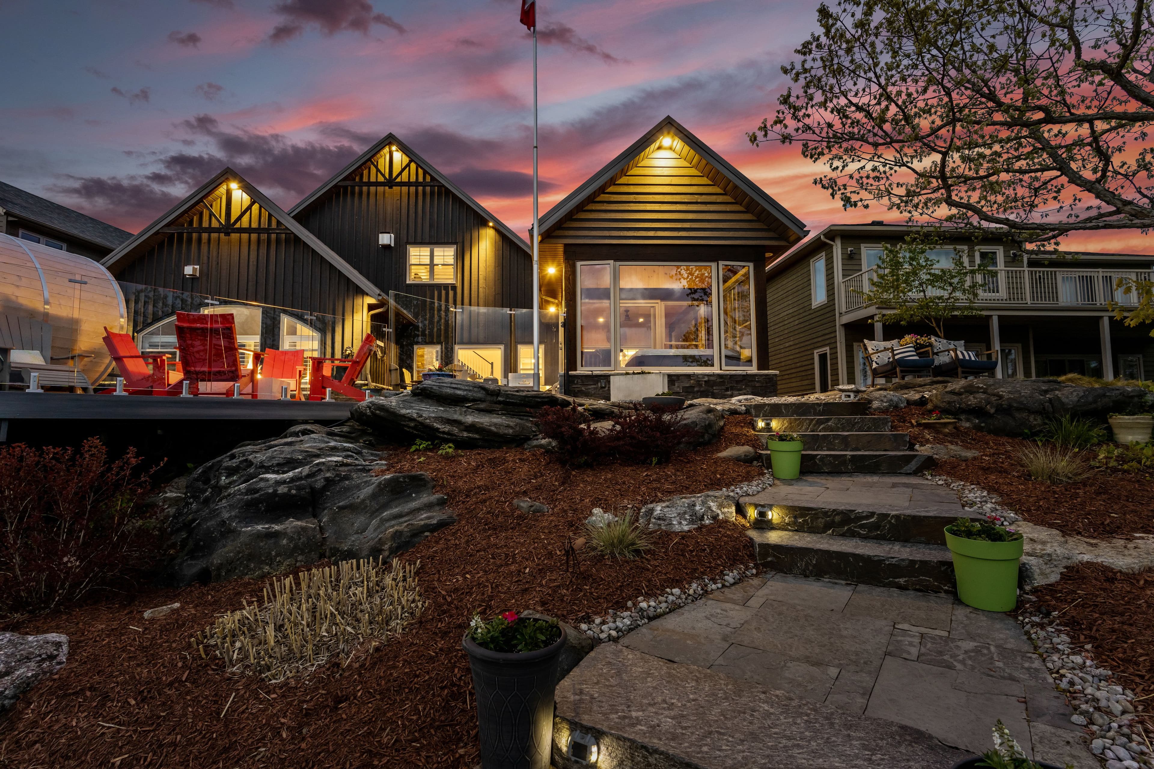 Waterfront cottages glowing at dusk with a stone path and landscaped gardens.